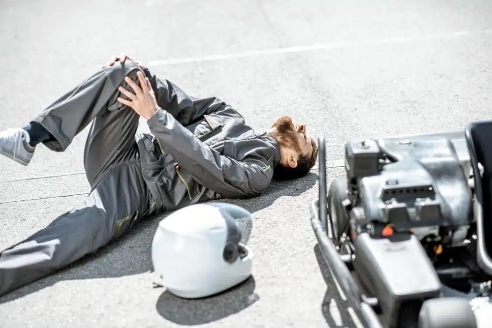 Motorcycle rider lying on road holding injured knee after auto accident representing knee injury claims in New York