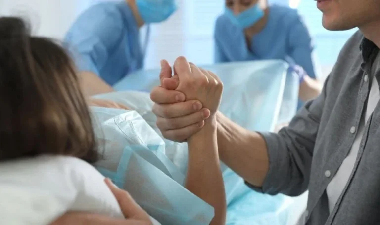 Husband holding his wife's hand during childbirth as medical staff assist in the delivery room — birth injury lawyer NYC