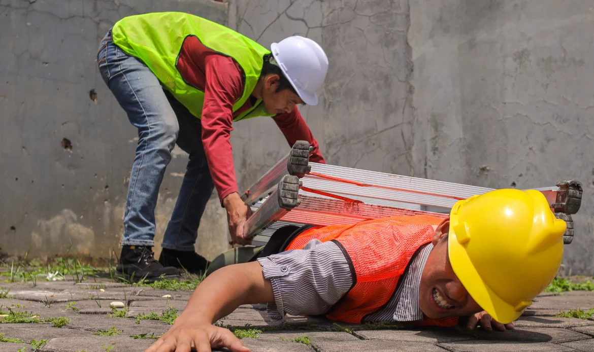 Construction worker lying on ground after fall from height, coworker moving ladder away — NY Labor Law 240 scaffold accident