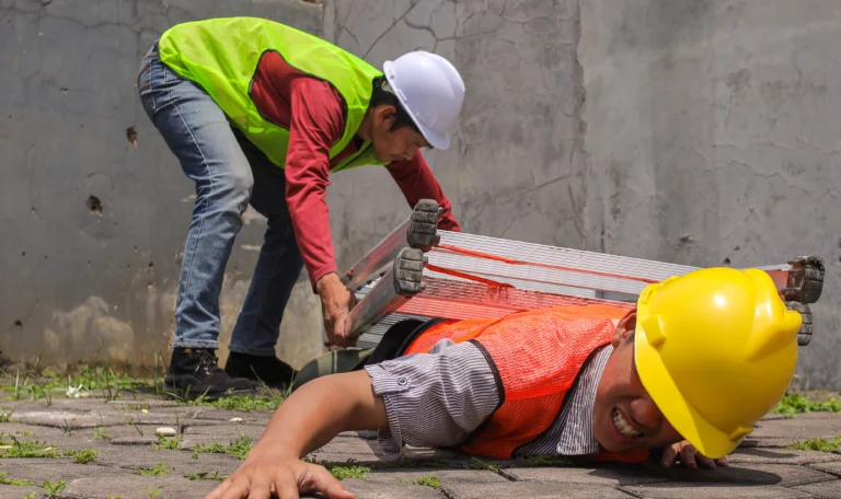 Construction worker lying on ground after fall from height, coworker moving ladder away — NY Labor Law 240 scaffold accident
