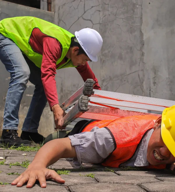 Construction worker lying on ground after fall from height, coworker moving ladder away — NY Labor Law 240 scaffold accident